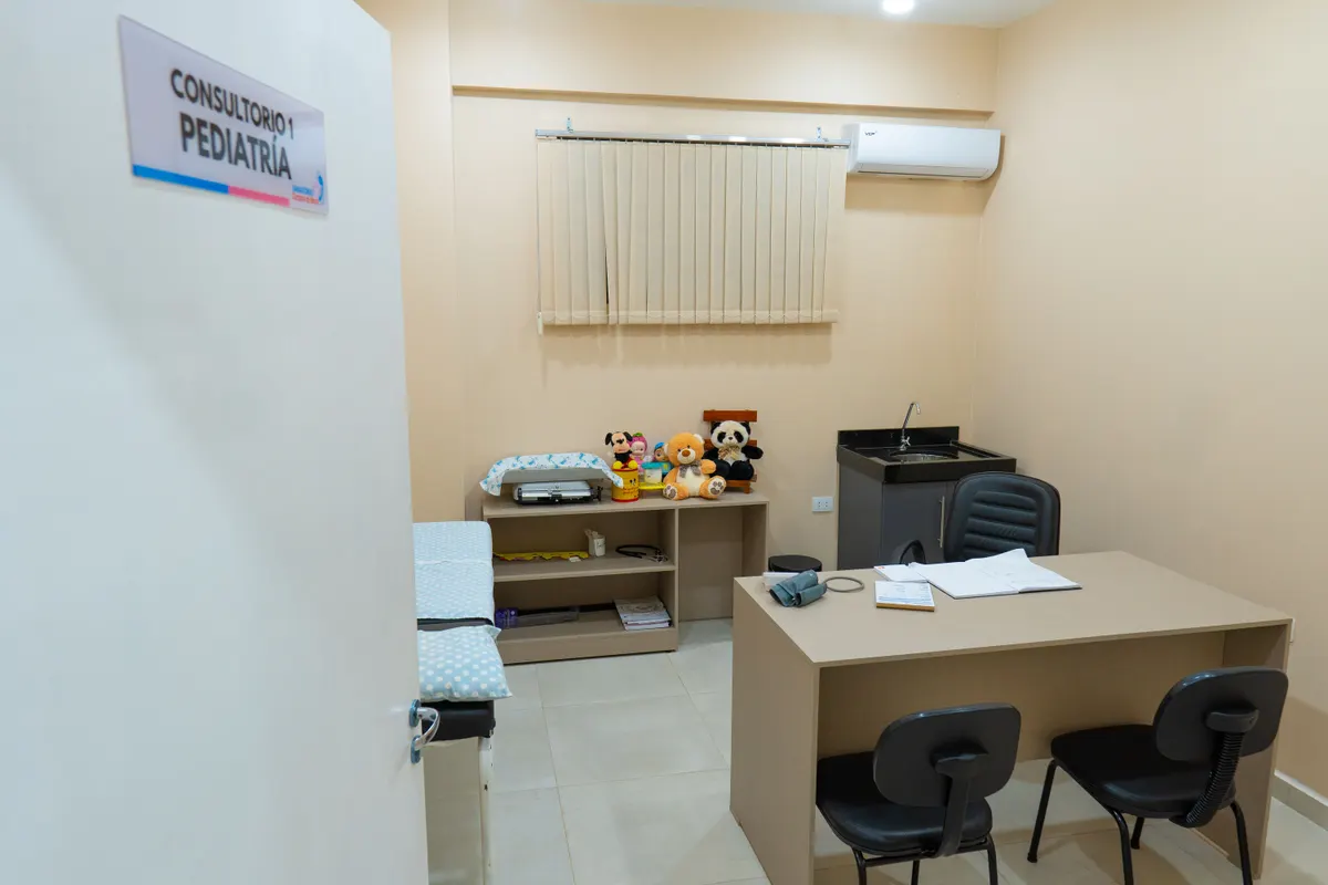 Consultorio de pediatría con camilla, escritorio y peluches